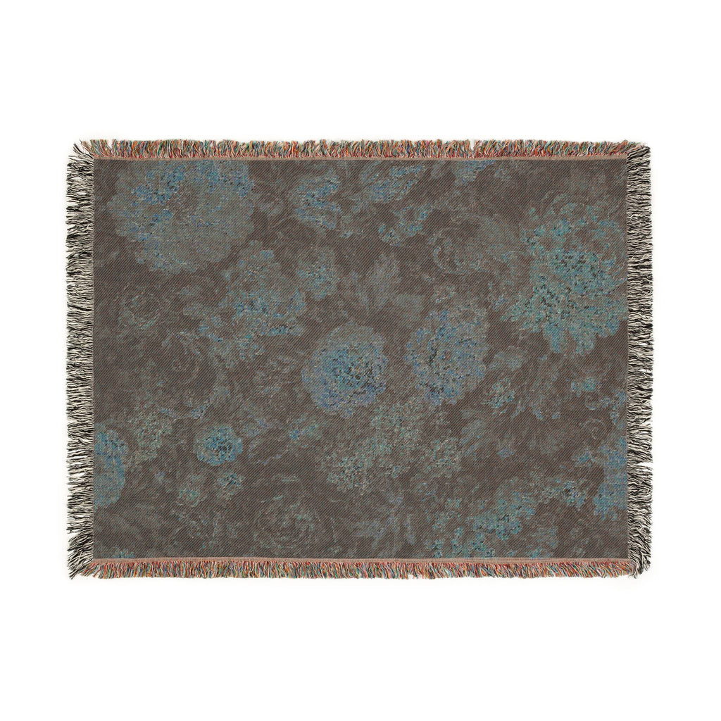 A rectangular woven throw blanket with fringed edges, featuring an abstract floral pattern in shades of brown, gray, and teal blue on a white background.