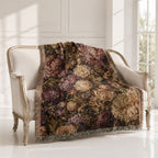 A vintage-style floral throw blanket draped over an antique cream armchair in a bright, sunlit room with white paneled walls and a window.