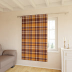A single window curtain panel with a brown, orange, and beige plaid pattern hanging on a silver rod in a bright living room.