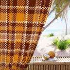 A close-up of a brown, orange, and beige plaid fabric panel draped over a bamboo table, with a blurred tropical beach scene in the background featuring palm trees and a coconut on a small white plate.