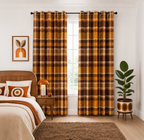 A pair of long window curtains in a warm mustard yellow, brown, and black plaid pattern, hanging on a black rod in a styled bedroom setting.