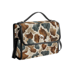 A structured handbag with a brown, beige, and gray watercolor cow print pattern, featuring black leather trim, a top handle, and a front flap with a silver-tone snap button.