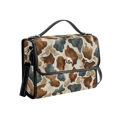 A structured handbag with a brown, beige, and gray watercolor cow print pattern, featuring black leather trim, a top handle, and a front flap with a silver-tone snap button.