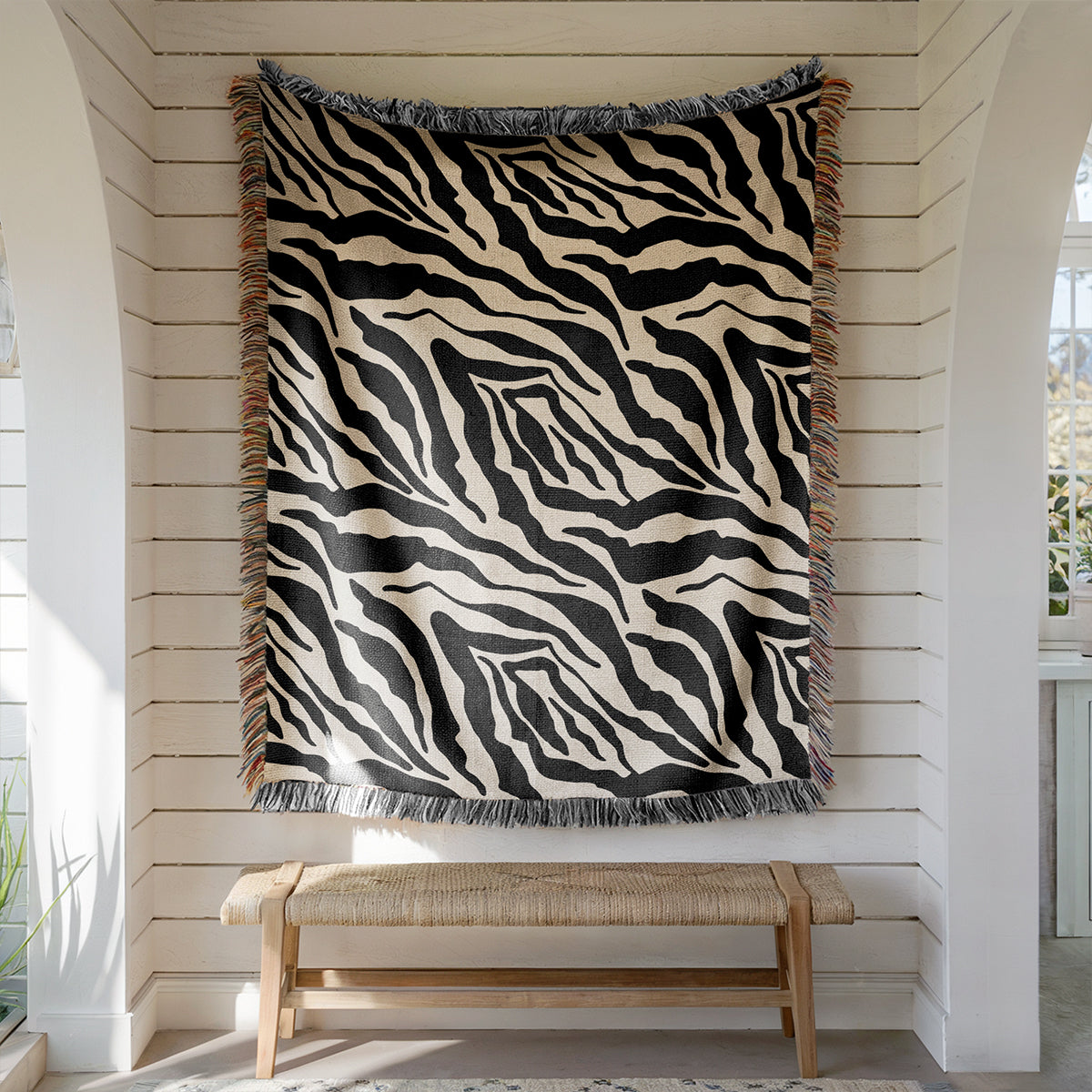 Zebra patterned throw blanket hanging on a white wall above a wooden bench.