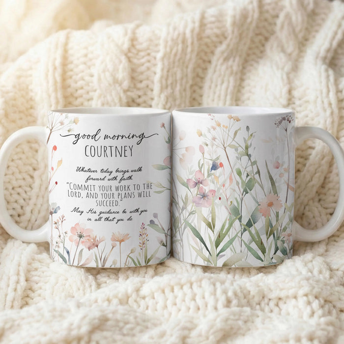 Two white ceramic mugs with floral and inspirational text designs, displayed side-by-side on a cozy cream-colored cable-knit blanket.